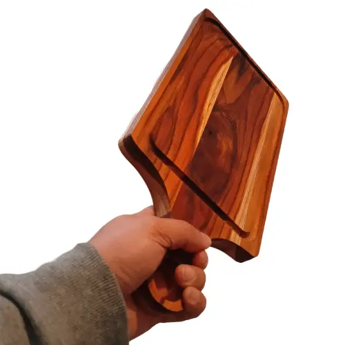 Mano de un hombre sosteniendo firmemente por el mango una gruesa tabla de madera de teca rectangular.