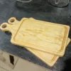 Dos tablas rectangulares de pino con mango apiladas sobre un banco de trabajo oscuro en un taller.