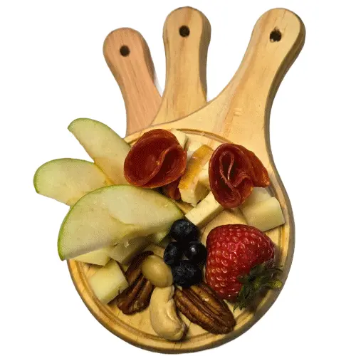 Mini tabla de madera circular sirviendo una porción individual de quesos, carnes frías, manzana, fresa y nueces.