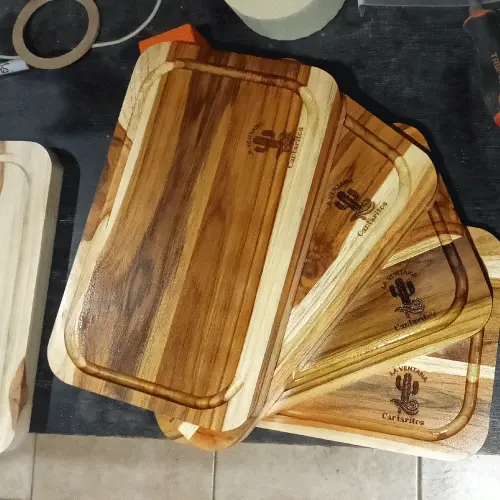Lote de cuatro tablas de madera recién grabadas con logo apiladas sobre un banco de trabajo en el taller.