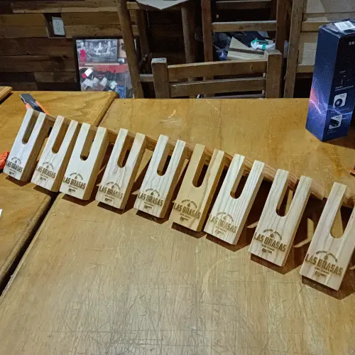 Múltiples servilleteros de madera grabados en serie de forma idéntica con el logotipo de Las Brasas, alineados sobre una mesa.