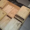 Vista de un taller con múltiples pilas de tablas rectangulares de pino, listas para entrega con diferentes nombres y logotipos grabados.