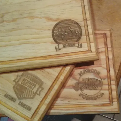 Tres tablas rectangulares de pino apiladas mostrando diferentes grabados láser, incluyendo un despacho contable y logotipos de camiones.
