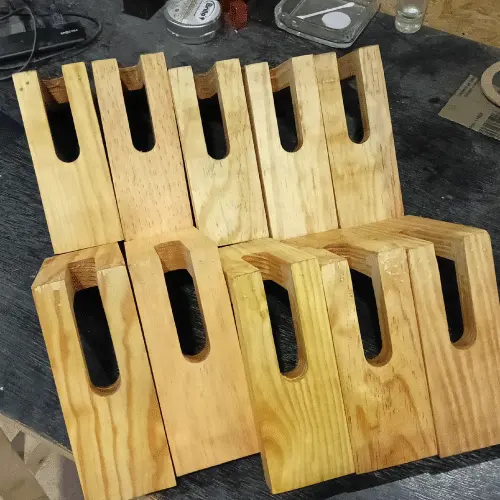 Fila de servilleteros triangulares de madera natural lisa con ranura superior, ordenados en un banco de trabajo.