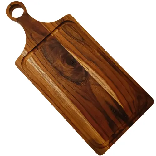 Tabla de madera de teca natural en ángulo diagonal, destacando un nudo oscuro en la veta central y el orificio redondo en el mango.