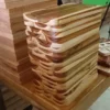 Pila muy alta de decenas de tablas rectangulares de madera de teca apiladas en un taller, mostrando su grosor uniforme.
