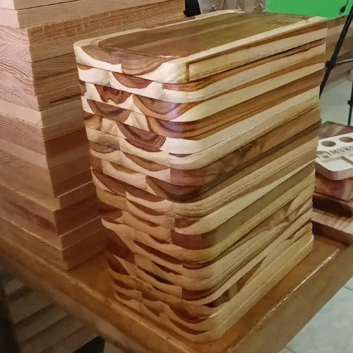 Pila muy alta de decenas de tablas rectangulares de madera de teca apiladas en un taller, mostrando su grosor uniforme.