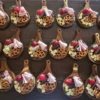 catering-mini-tablas-charcuteria-eventos-perspectiva2.webp Vista superior de múltiples mini tablas de madera circulares ordenadas en filas, listas con aperitivos de charcutería, fresas y pretzels.