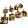 Surtido de cinco mini tablas de madera cuadradas presentadas con diferentes porciones de quesos, carnes frías, manzanas y pretzels.