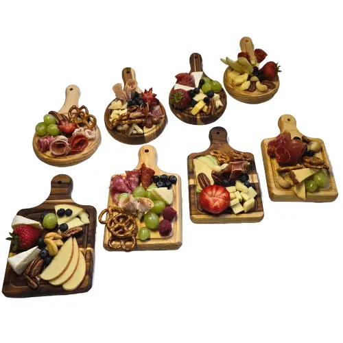 Surtido de cinco mini tablas de madera cuadradas presentadas con diferentes porciones de quesos, carnes frías, manzanas y pretzels.