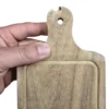 Mano mostrando una mini tabla de madera con un detalle o desportillado en el borde superior del mango.