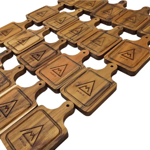 Mesa larga en un evento real llena de decenas de mini tablas de madera cuadradas, cada una servida de manera uniforme con charcutería.
