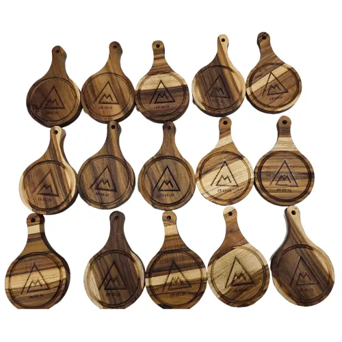 pedido-recuerdos-eventos-mini-tablas-grabadas.webp Quince mini tablas de madera redondas distribuidas en tres filas, todas con el mismo grabado láser de un logo y fecha para un evento.