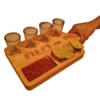 Mano sosteniendo una tabla de madera para tequila de Santos Customs Designs, equipada con 4 caballitos de vidrio, chile, limón y un grabado de las Fases del Tequila.